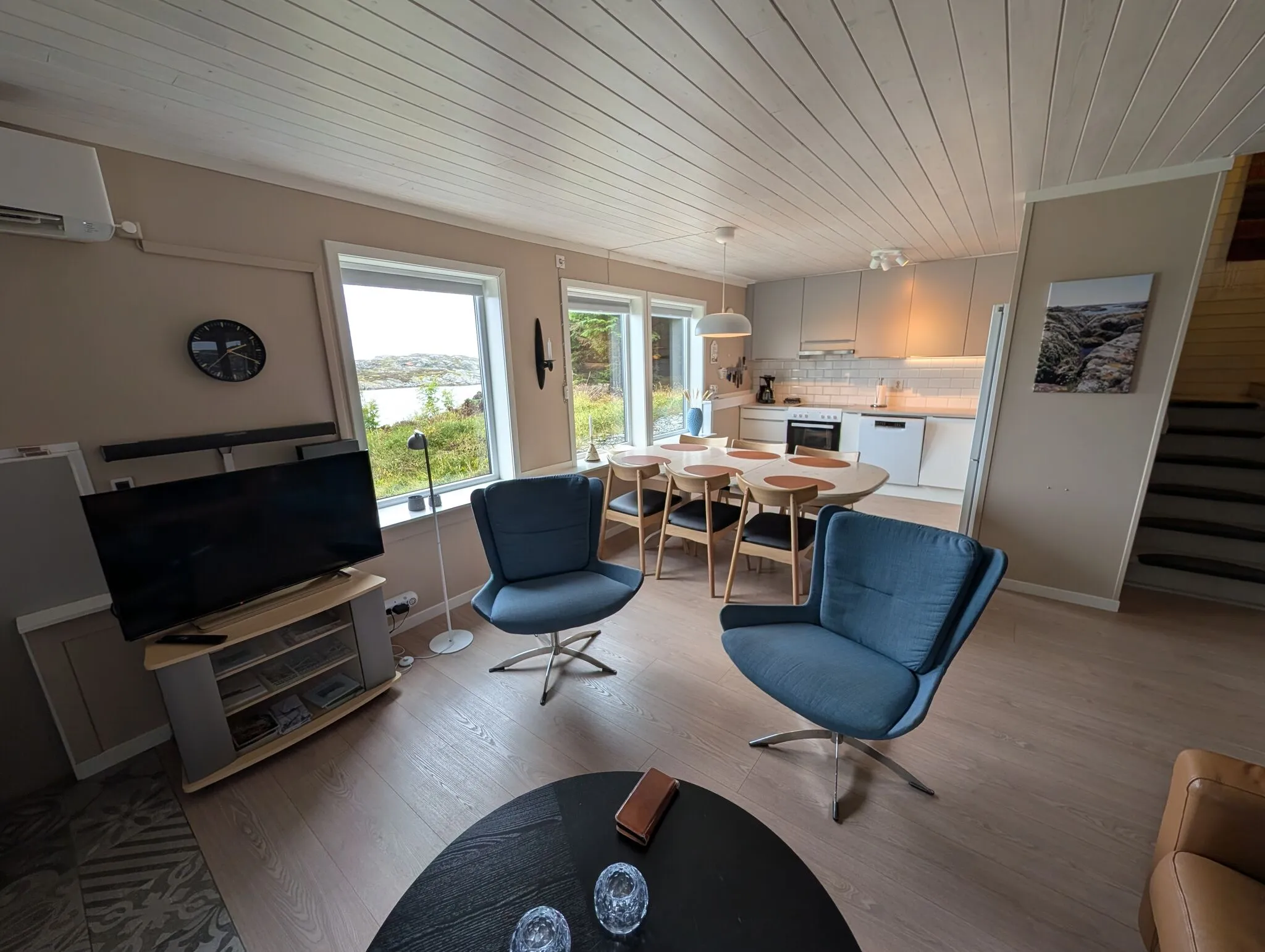 Åpen stue- og kjøkkenløsning med spisebord, hvitt kjøkken og trapp til andre etasje